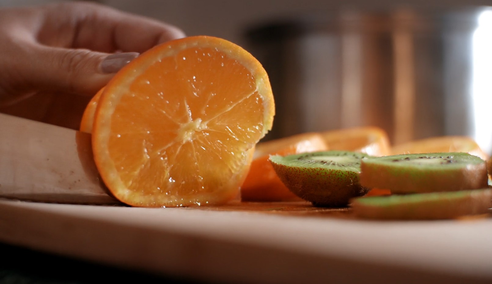 Person cuts orange and kiwis on a cutting board