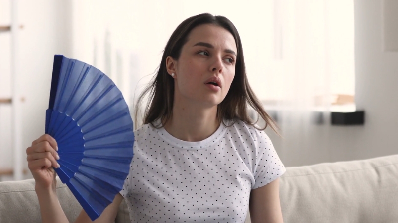 Woman fanning herself to reduce heat and humidity that worsen Malassezia yeast