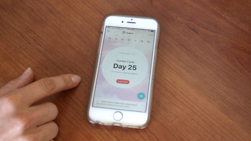 A person uses a smartphone period tracking app that shows the current cycle day on the screen